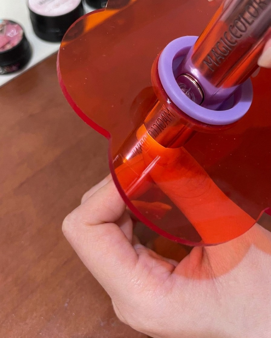 Un ongle en train de catalyser sous une petite lampe UV/LED rose portable.