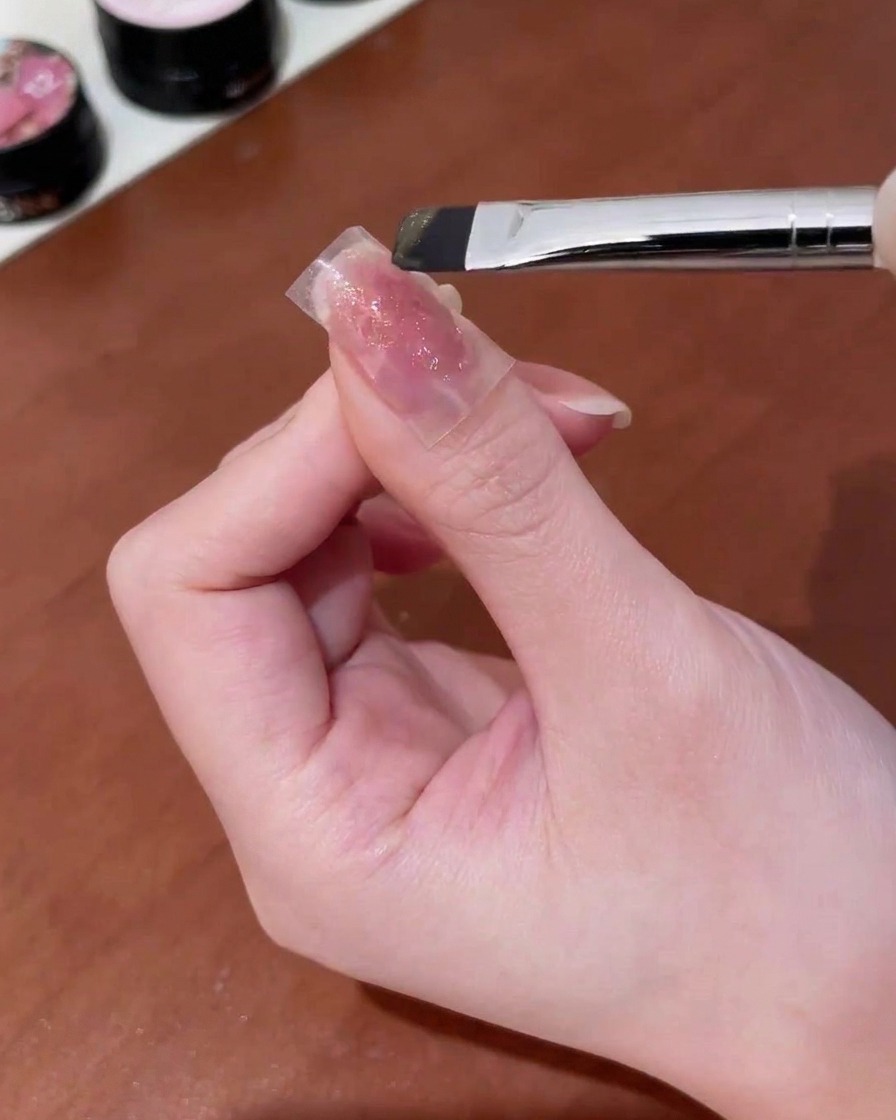 Un pinceau appliquant du gel cat-eye or sur un autocollant papillon sur un ongle.
