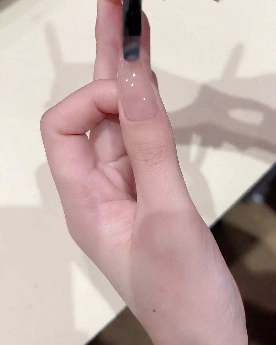 Gros plan dun pinceau à ongles appliquant une fine couche uniforme de gel nude transparent sur un ongle déjà recouvert dune base.