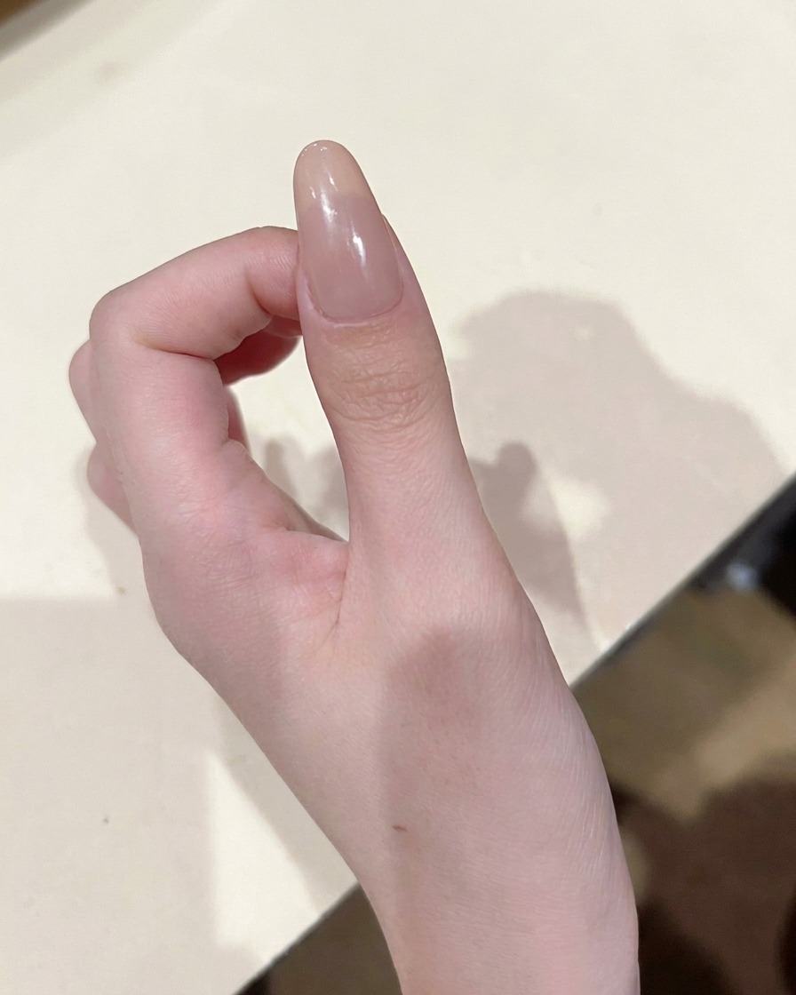 Gros plan dun pinceau de précision déposant un petit point de vernis gel rose au centre dun ongle nude.