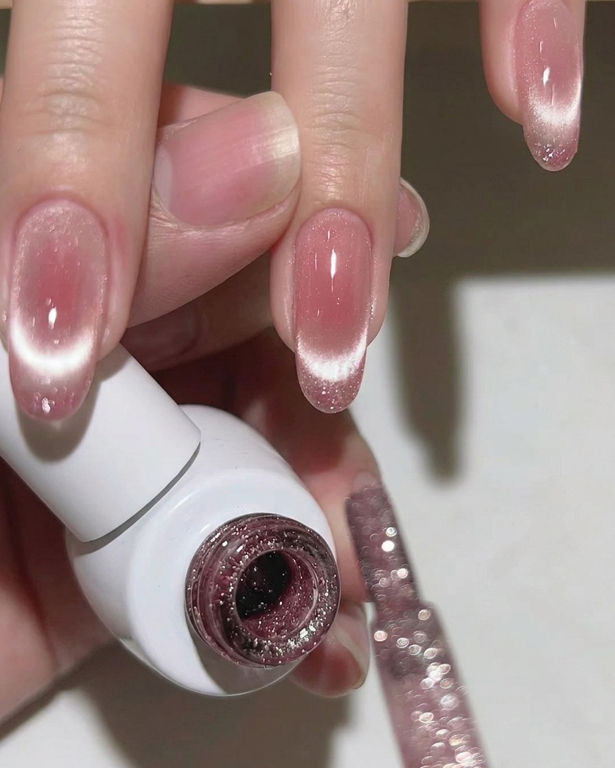 Gros plan sur un ongle montrant une ligne scintillante cat-eye centrée sur la pointe sur une base rose.