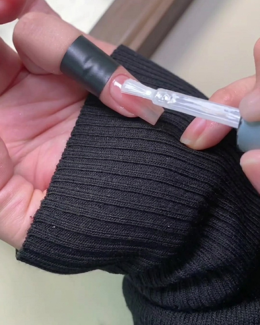 Pinceau appliquant un top coat brillant sur un ongle rose.