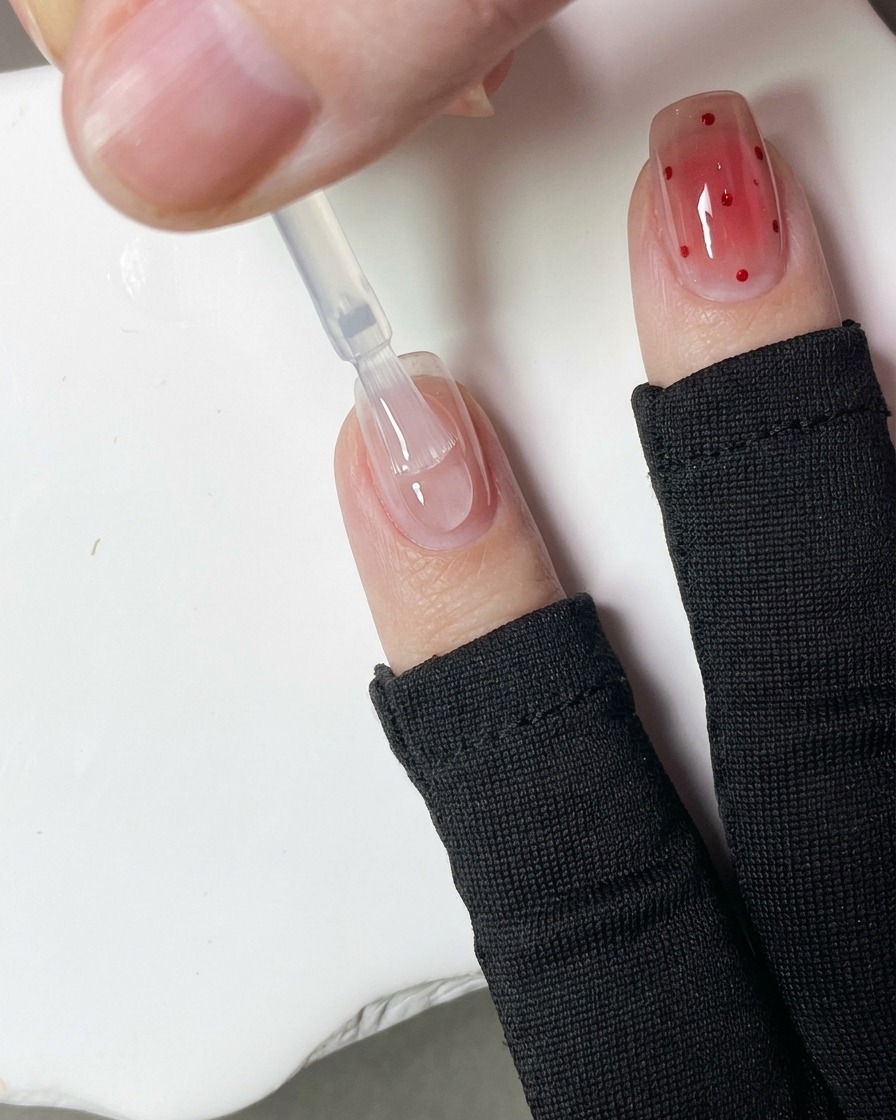 Gros plan dun dotting tool appliquant de petits points de gel rouge sur la surface dun ongle.