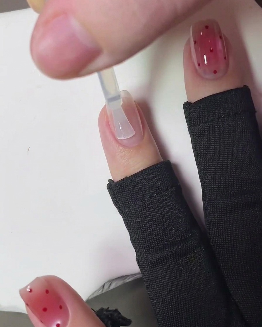 Un pinceau appliquant un top coat transparent et brillant sur le nail art strawberry blush terminé.