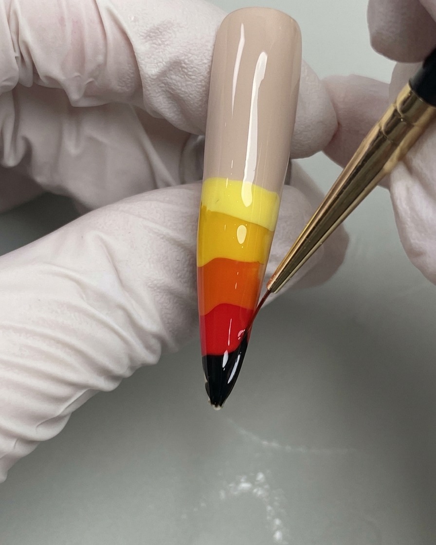 Un pinceau liner fin tirant les couleurs de gel humides vers le haut pour créer des flammes.