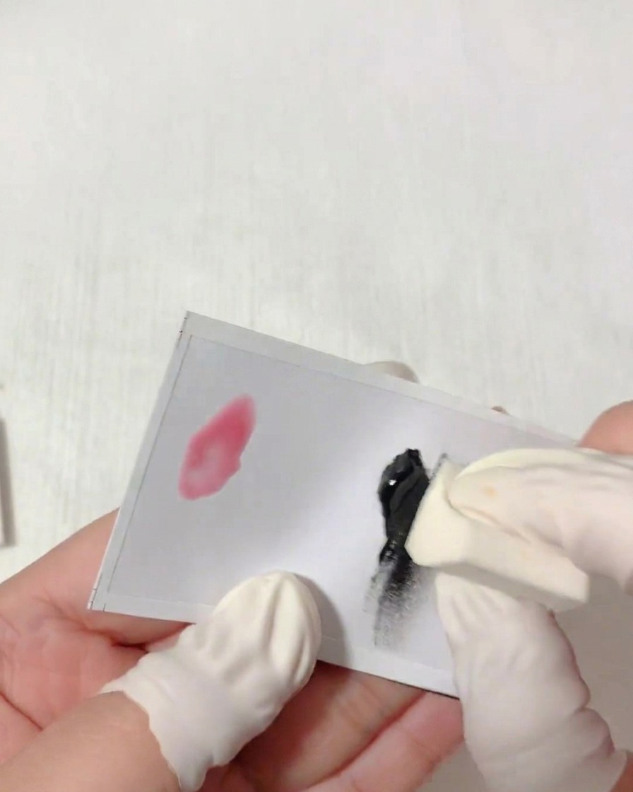 Vue rapprochée dune main portant un doigtier tapotant une éponge triangulaire dans du gel noir sur une palette blanche.