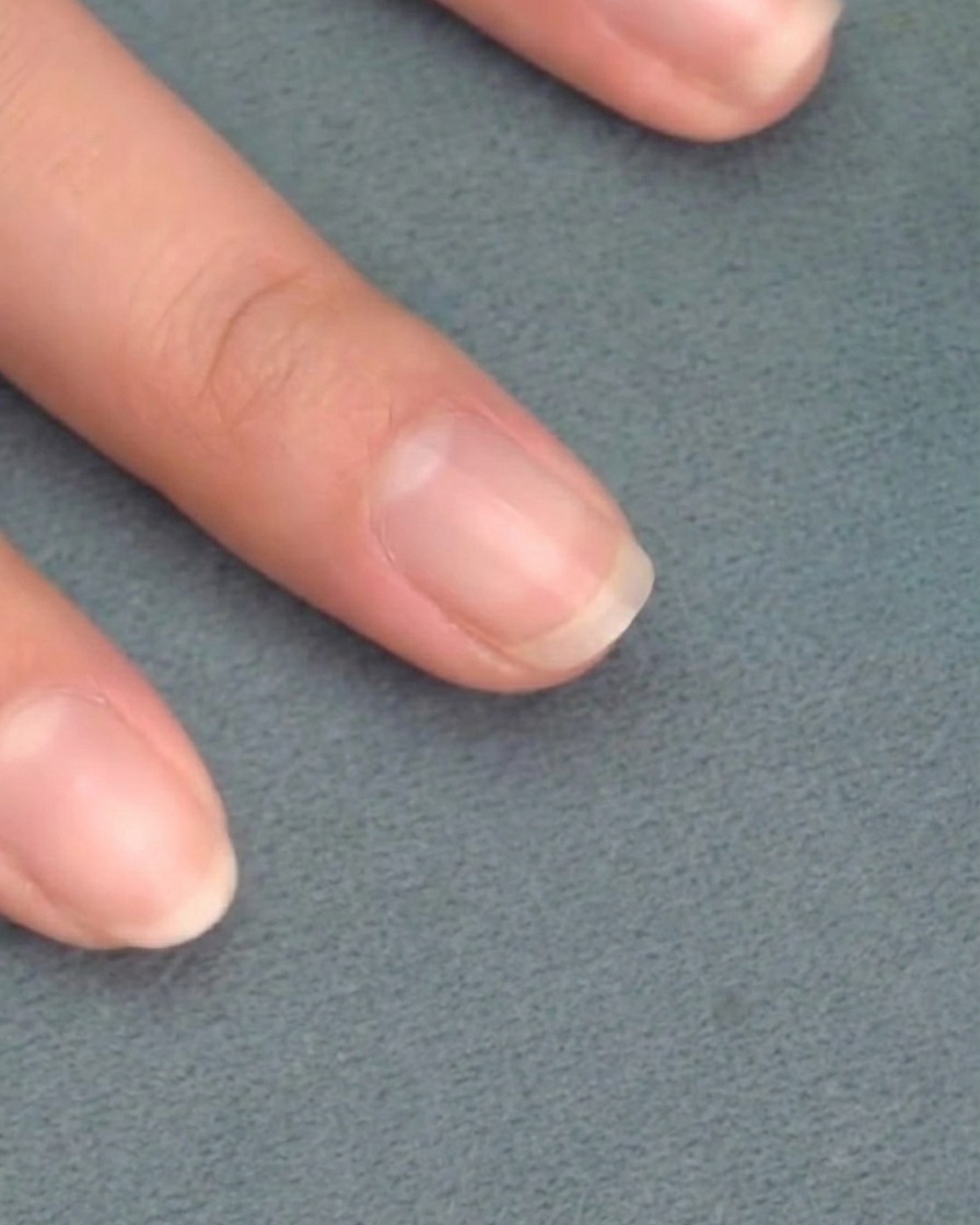 Pinceau appliquant un gel de base rose transparent sur un ongle naturel propre.