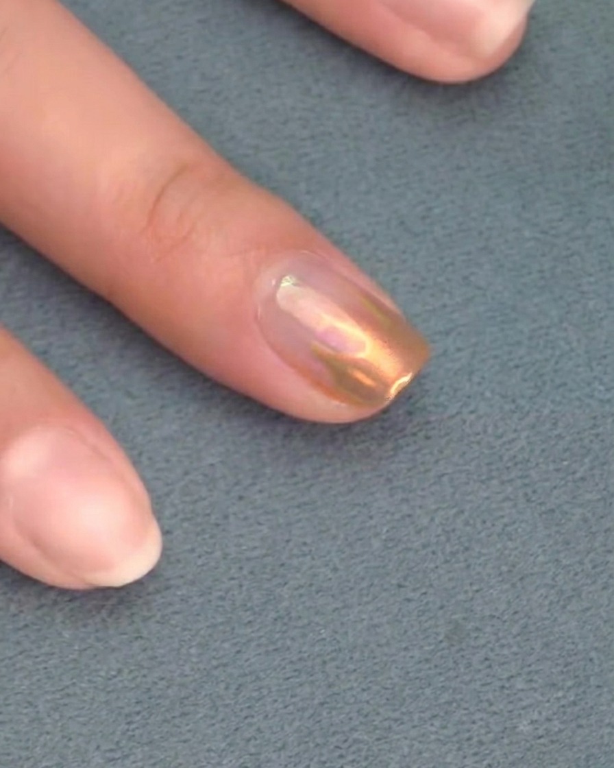 Pinceau appliquant un top coat transparent final sur un ongle aux détails chromés.