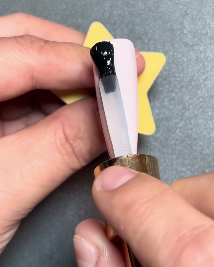 Un pinceau appliquant une ligne de vernis gel noir horizontalement sur la pointe dun ongle rose.
