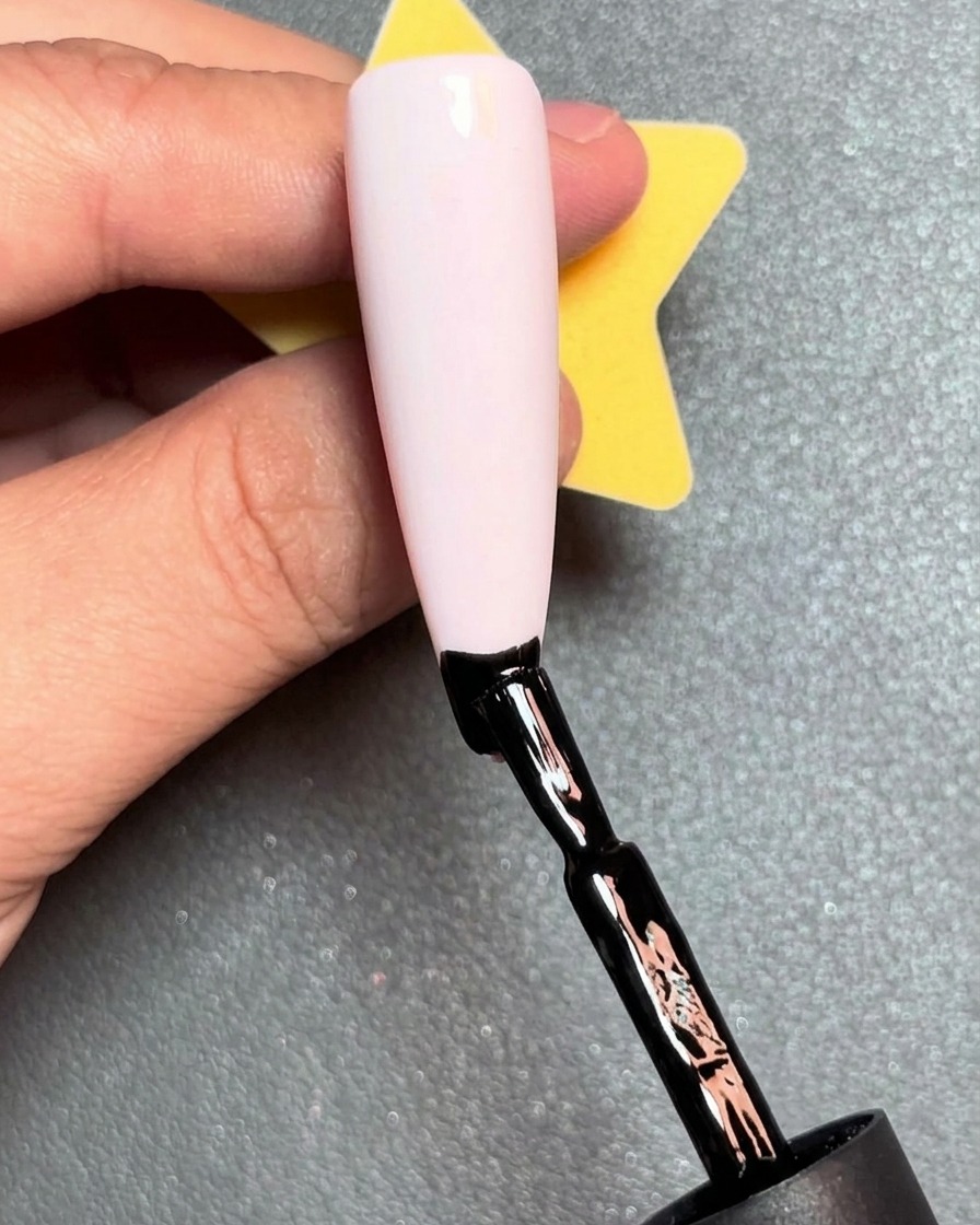 Un pinceau appliquant une ligne de vernis gel rouge juste au-dessus de la ligne noire sur un ongle.