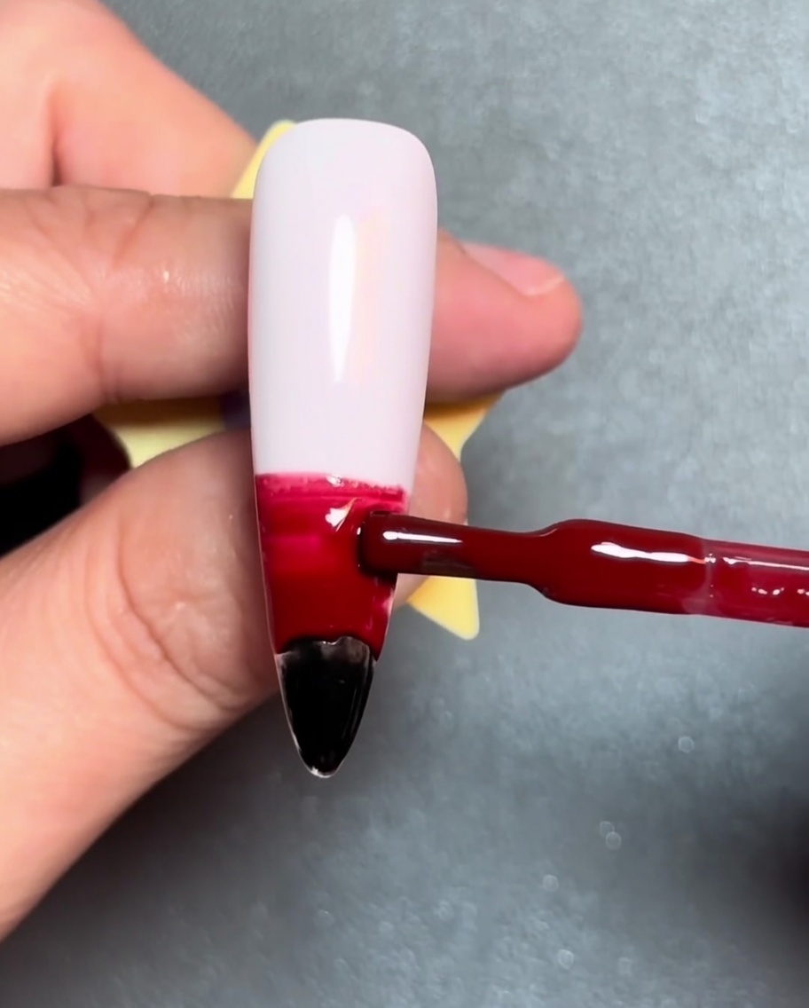 Un pinceau appliquant une bande horizontale de vernis gel orange au-dessus du rouge.