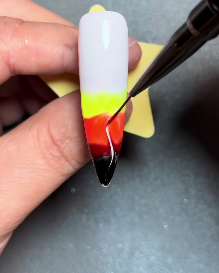 Gros plan montrant un pinceau liner traçant des lignes de couleur vers le haut à travers le gel humide, créant des formes de flammes.