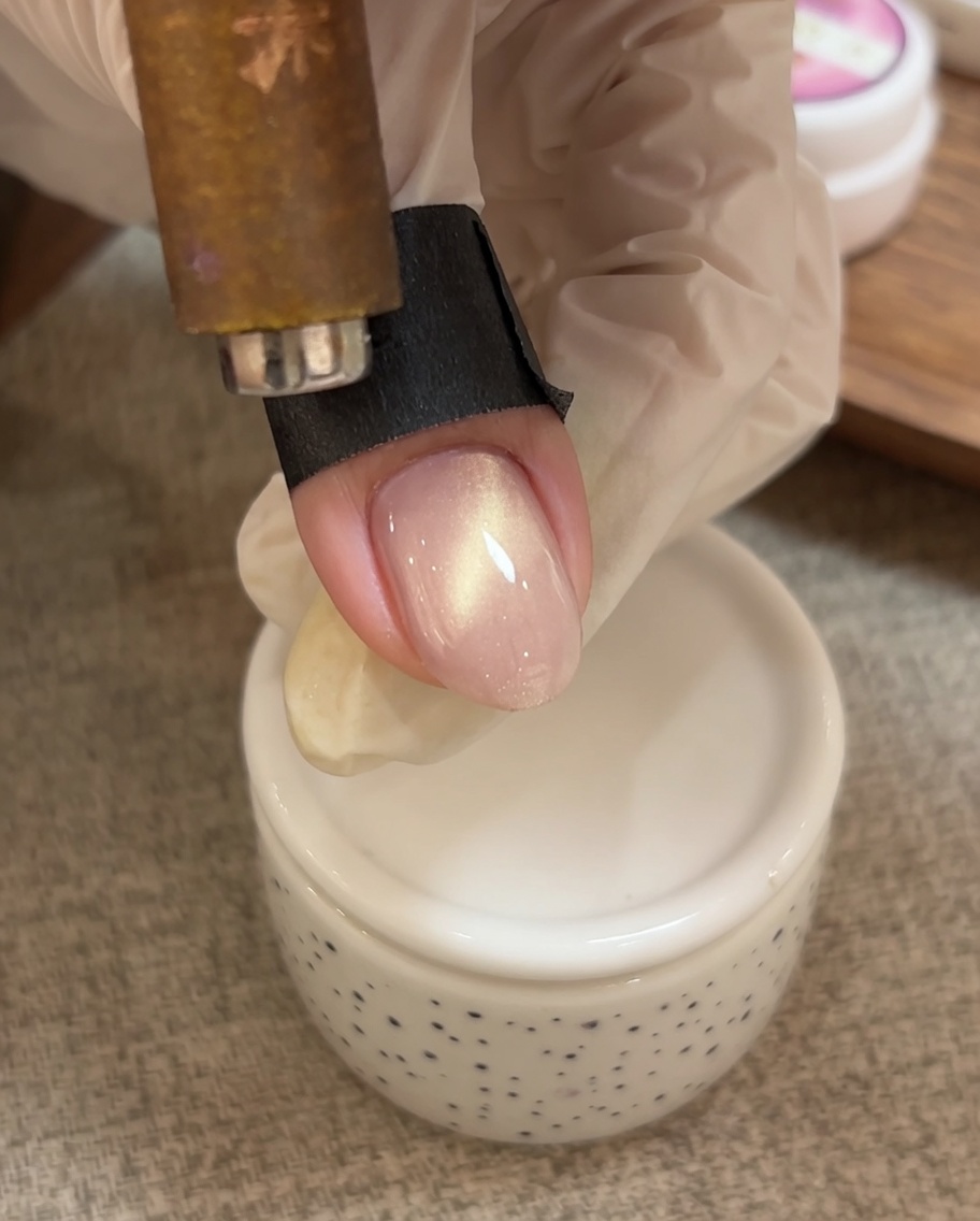 Une main utilise un aimant pour diriger les particules scintillantes du gel cat eye vers le bord libre de longle.