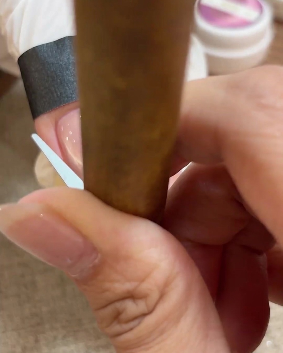 Gros plan sur un outil utilisé pour façonner le gel cat eye en un arc parfait de french manucure sur longle.