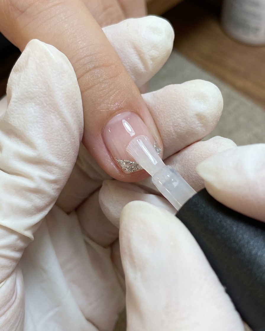 Un pinceau applique une couche de top coat transparent sur un ongle décoré dun cœur et de lignes blanches et argentées.