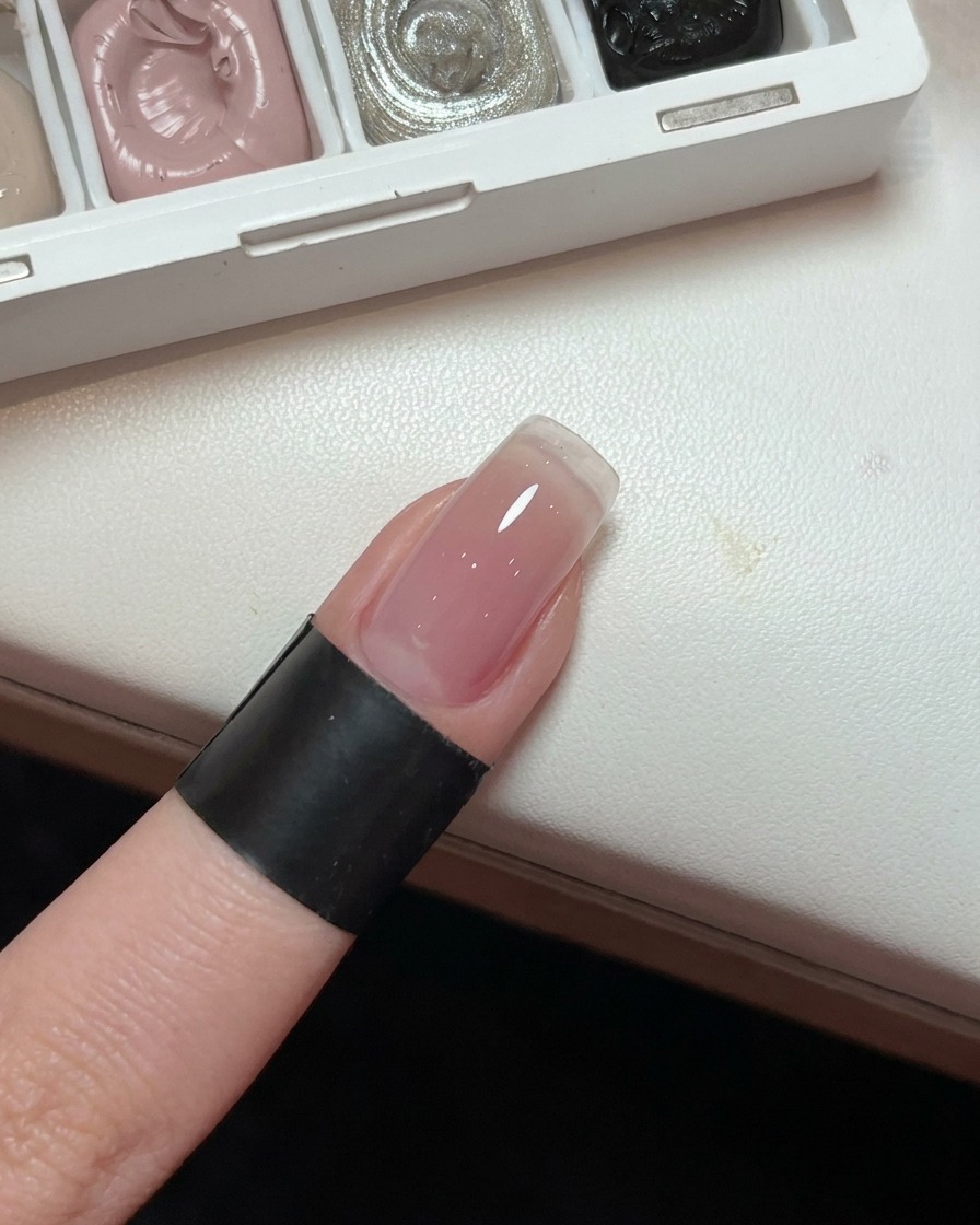 Un gros plan dun ongle montrant une base de gel en dégradé rose clair et lisse.