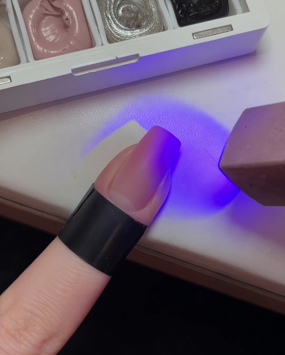 Un ongle avec une base en dégradé rose clair en train de catalyser sous une lampe UV violette.