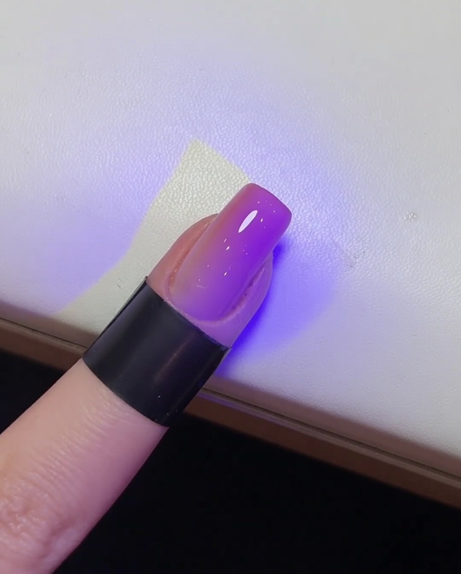 Un gros plan dun ongle brillant et fini en train de catalyser sous une lampe UV.