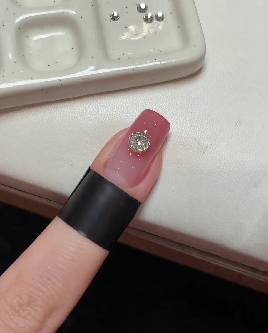 Le cristal principal posé sur un ongle rose, positionné sous un éclairage UV.