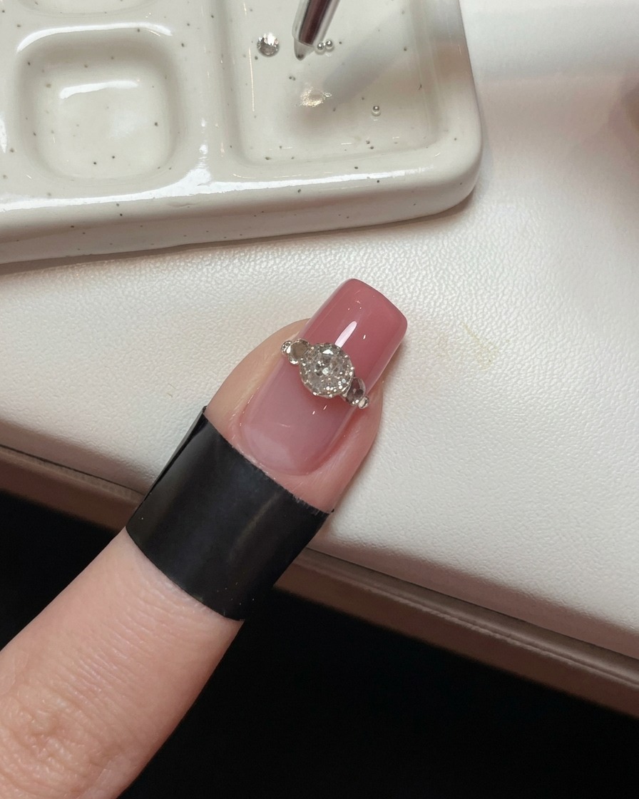 Un gros plan dun ongle avec un grand cristal, montrant un outil de précision plaçant de minuscules billes en acier autour de sa base pour créer un effet de griffes.