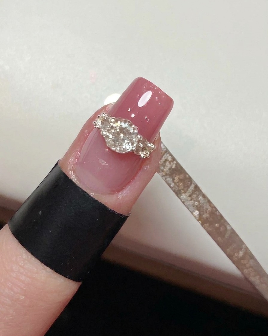 Un pinceau liner fin peignant soigneusement du top coat autour de la base dun design de bague en cristal terminé sur un ongle rose.
