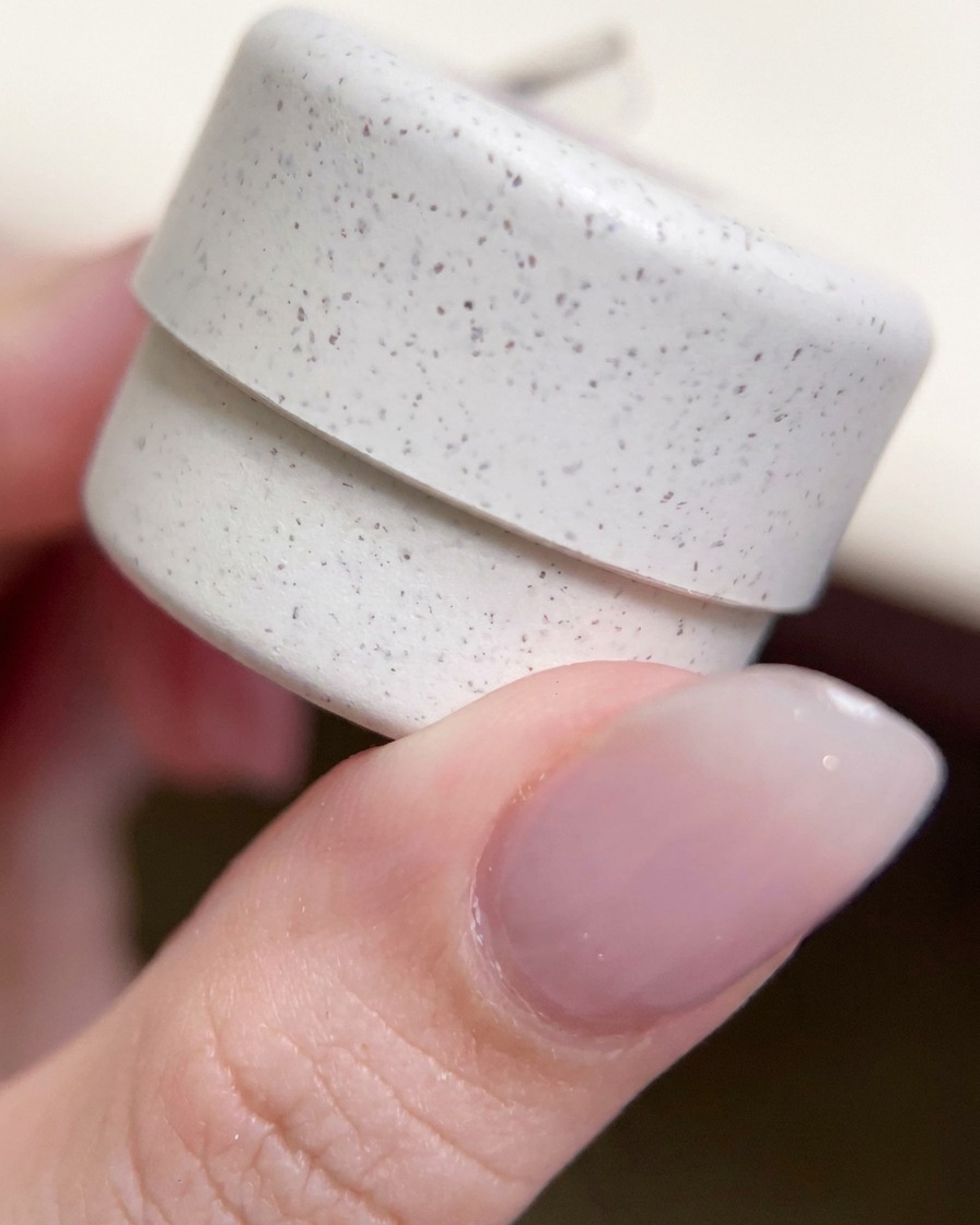 Gros plan sur un pot de vernis gel pailleté décoratif tenu entre les doigts.