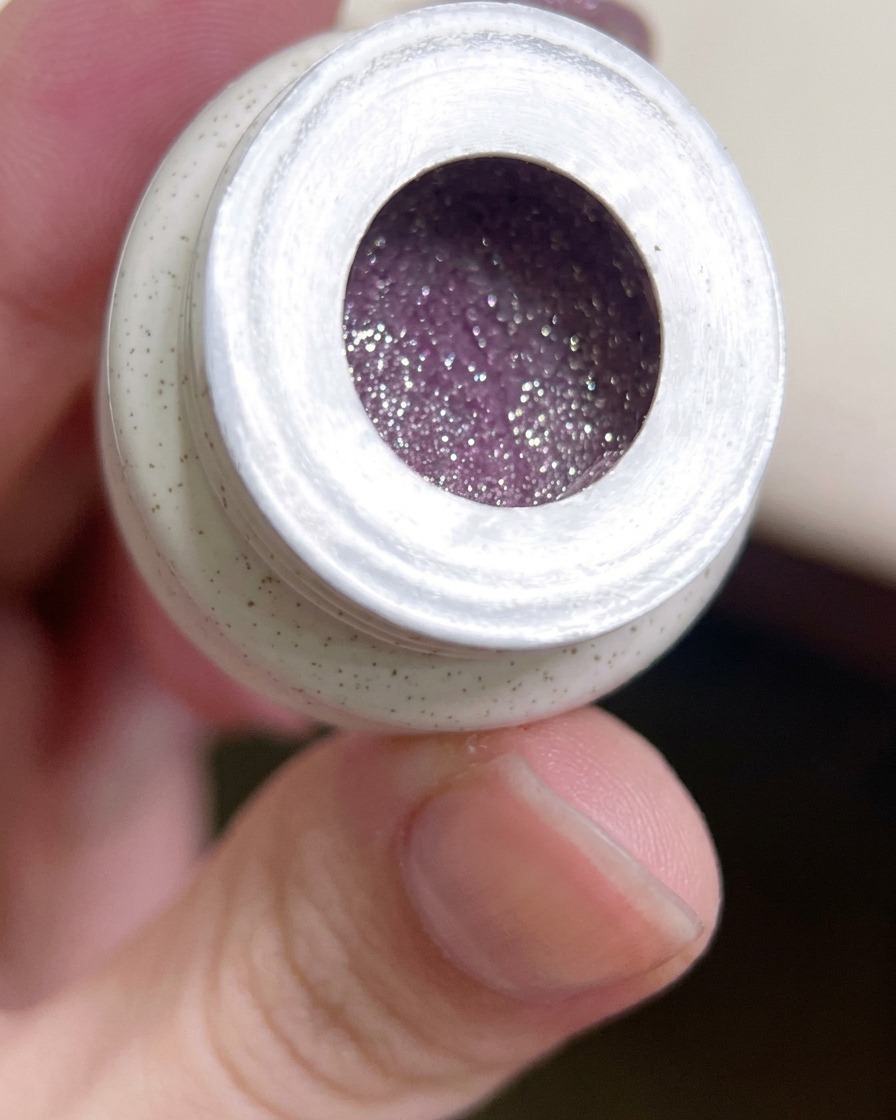 Un pinceau gel plat plongeant dans un pot de vernis gel violet intense et pailleté.