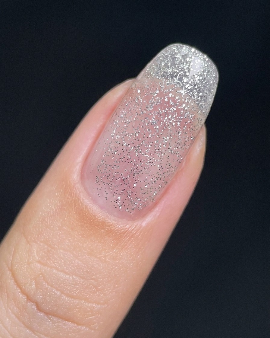 Un ongle recouvert dune fine couche translucide de gel pailleté argenté.