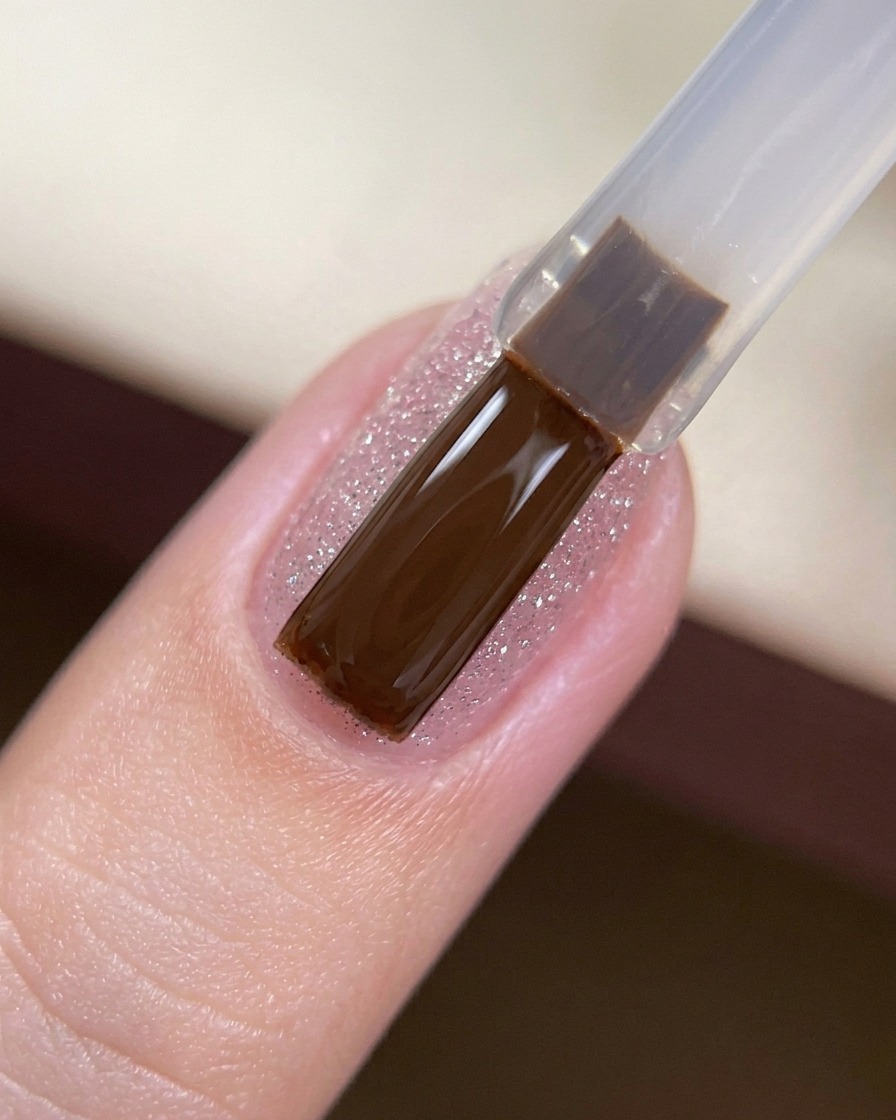 Un pinceau gel appliquant une couche de finition transparente et brillante sur un ongle pailleté.