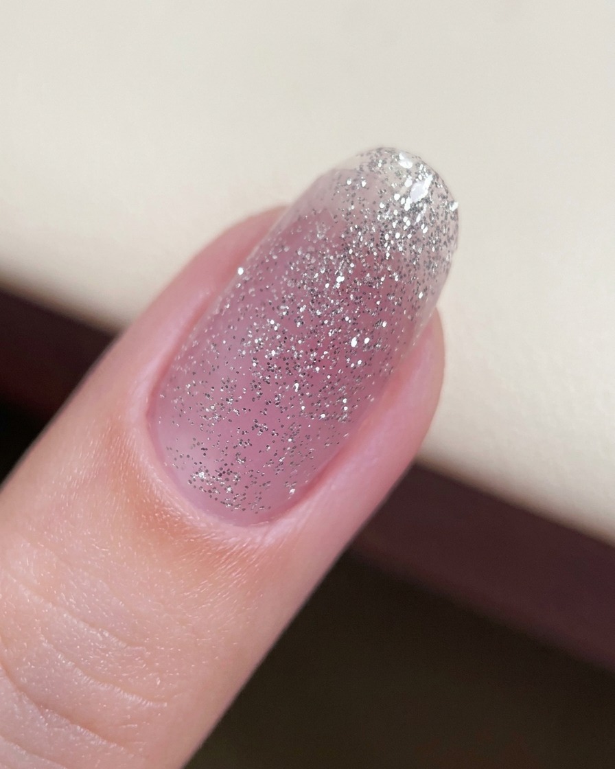 Gros plan sur un ongle avec une fine couche de base de gel pailleté appliquée.