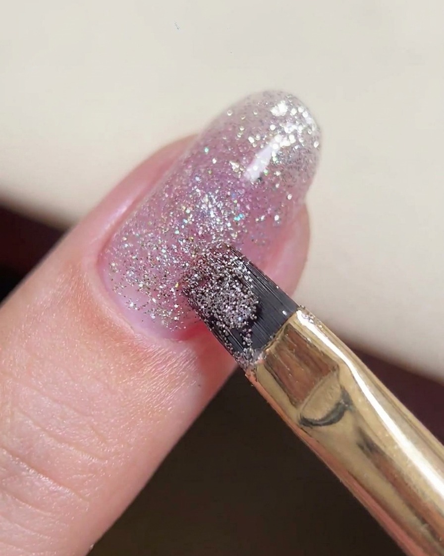 Un pinceau gel manipulant une plus grosse perle de gel pailleté au centre de longle.