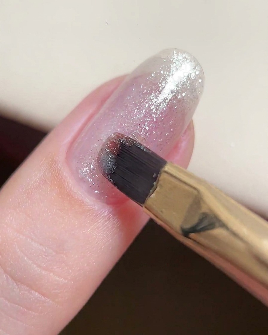 Un pinceau gel appliquant une couche fine et homogène de gel pailleté argenté sur un ongle naturel.