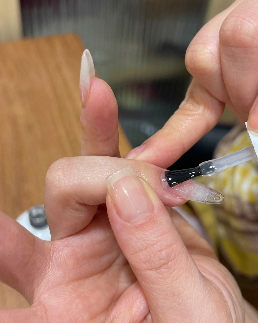 Un pinceau appliquant un top coat brillant sur un ongle texturé cat-eye.