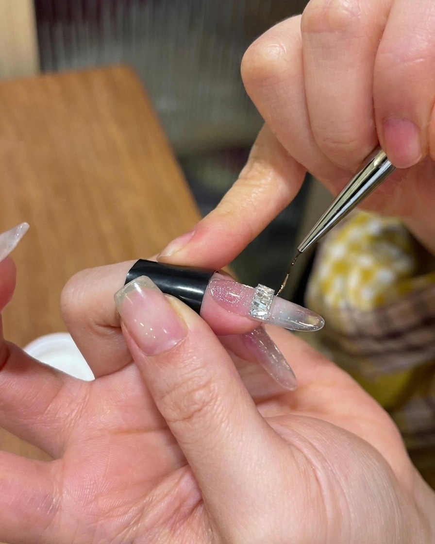 Un pinceau liner fin appliquant du gel top coat dur autour de la base dun strass argenté.