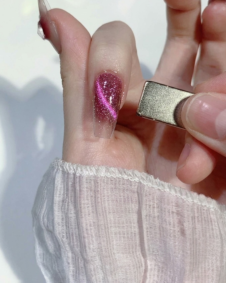 Aimant rectangulaire positionné sur le côté dun ongle rose pour aligner les paillettes.