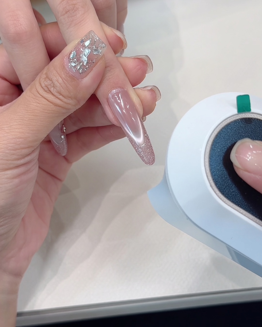 Une main placée sous la lampe de polymérisation, focus sur les ongles à pointes pailletées.