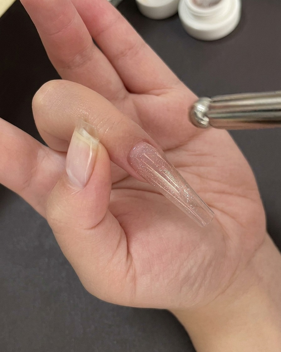 Une main positionnée sous une lampe UV/LED professionnelle catalysant la couche de base gel.