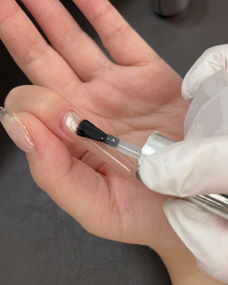 Un pinceau à ongles professionnel appliquant une couche de finition transparente et brillante sur une base gel cat-eye scintillante.