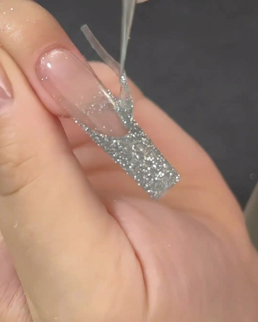 Une pince à épiler retirant un guide adhésif de French manucure dun ongle long, révélant une ligne nette.