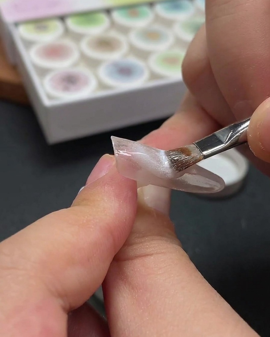 Gros plan montrant un aimant survolant un ongle pour déplacer les particules métalliques dans le gel cat-eye blanc humide.
