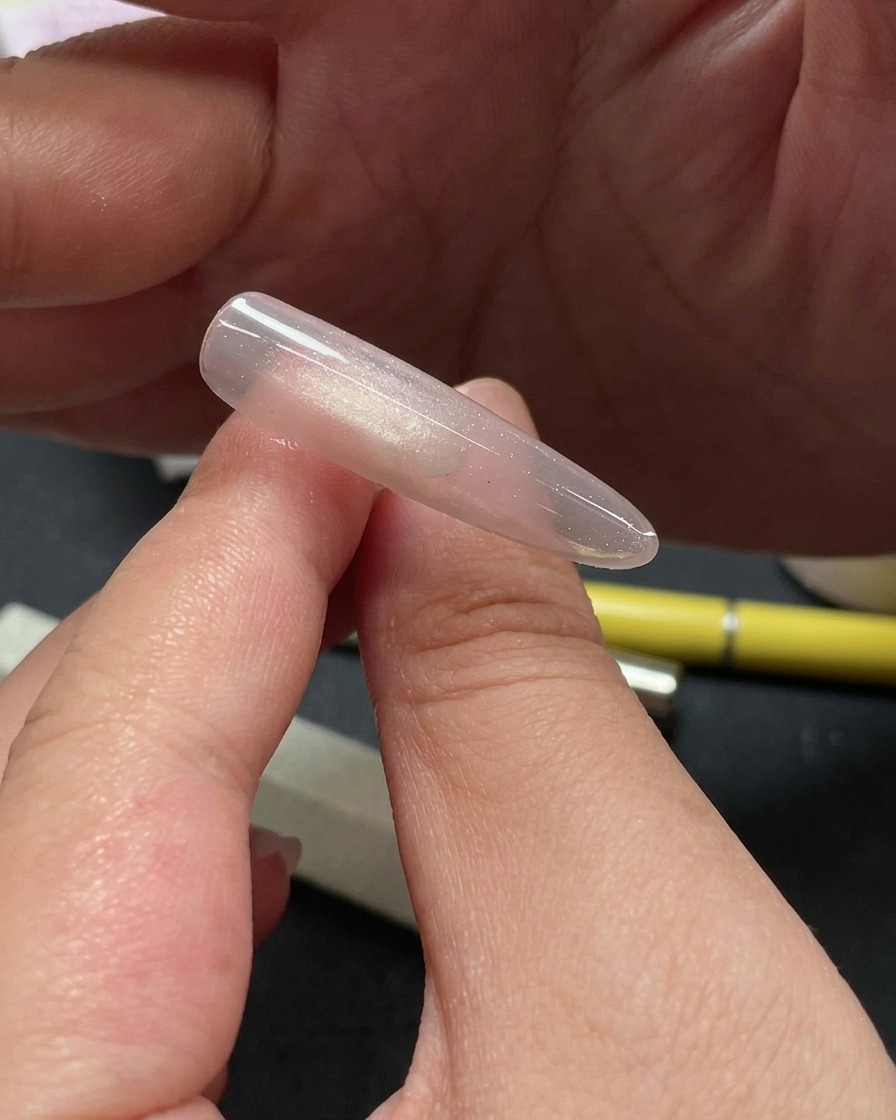 Gros plan dune main utilisant un outil pour placer de petits morceaux de paillettes scintillantes sur la partie supérieure dun ongle cat-eye.