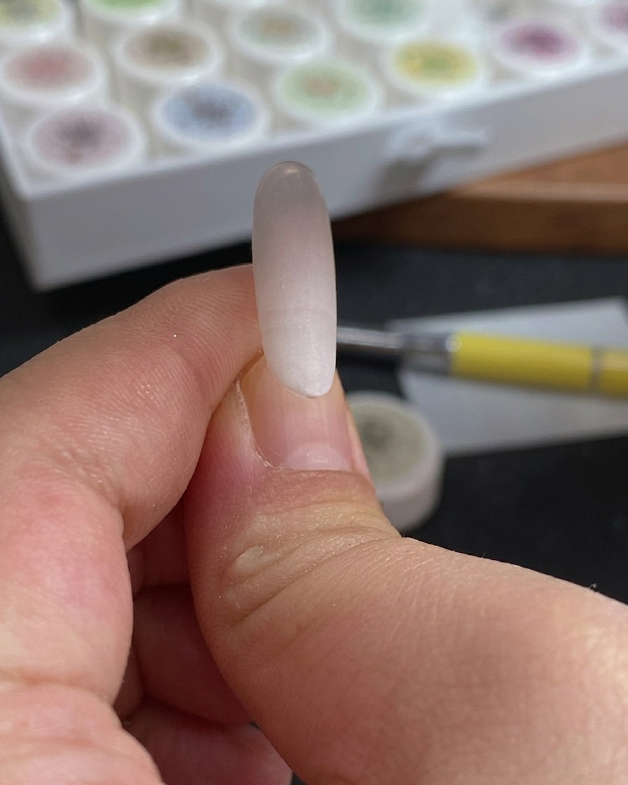 Gros plan dune éponge tamponnée sur le bout dun ongle pour créer un dégradé de couleur rose rouge et blanc.