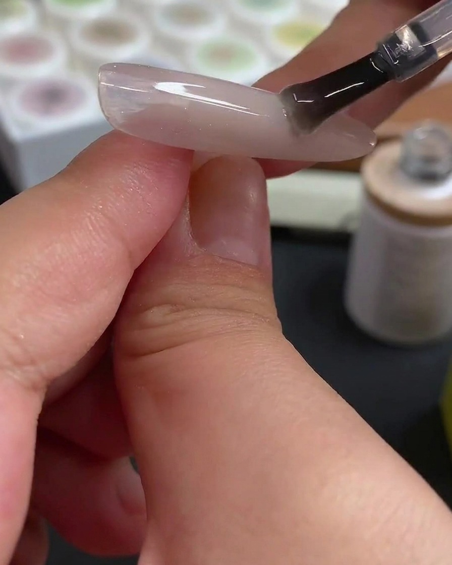 Un outil de dotting appliquant des pois de vernis rouge rosé précis sur une surface dongle préparée.