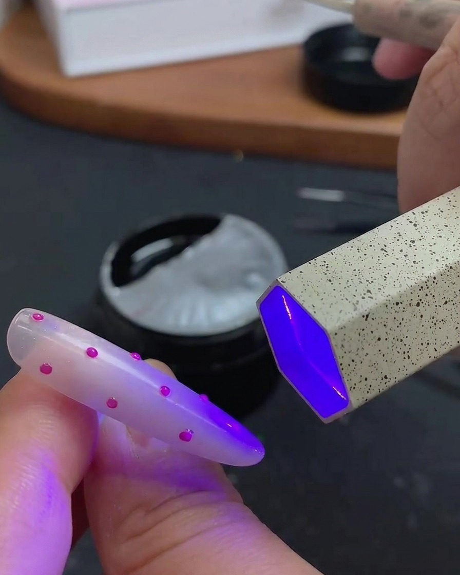 Un pinceau appliquant un top coat transparent brillant sur le nail art à pois 3D.