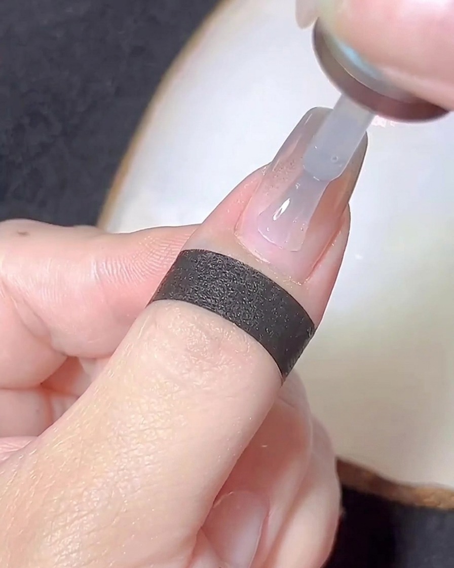 Un pinceau à ongles appliquant une fine couche de gel de base transparent sur un ongle saupoudré de chrome.