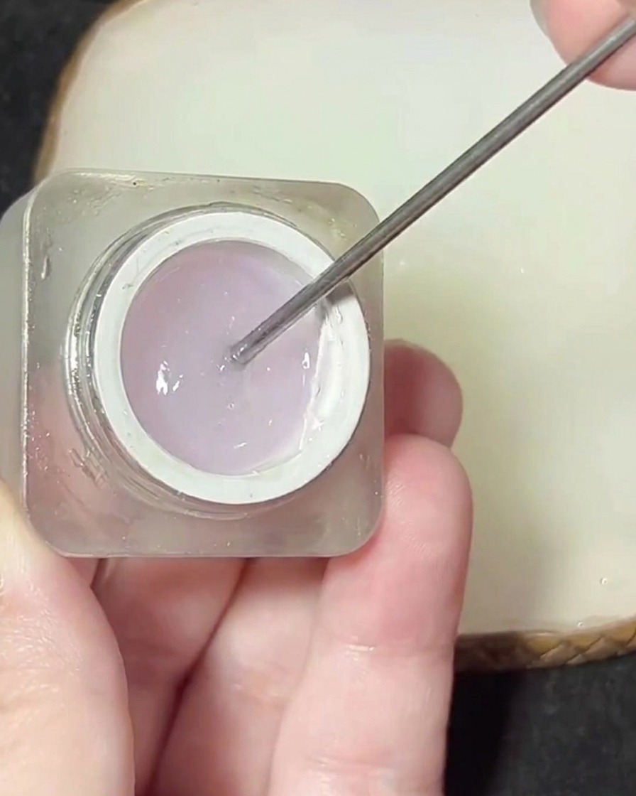 Une spatule en métal prélevant un produit gel épais et transparent dun petit pot.