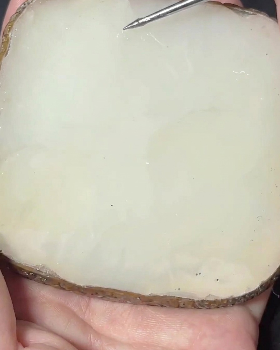 Une spatule en métal mélangeant un pigment rose dans une base de gel transparente sur une palette en pierre.