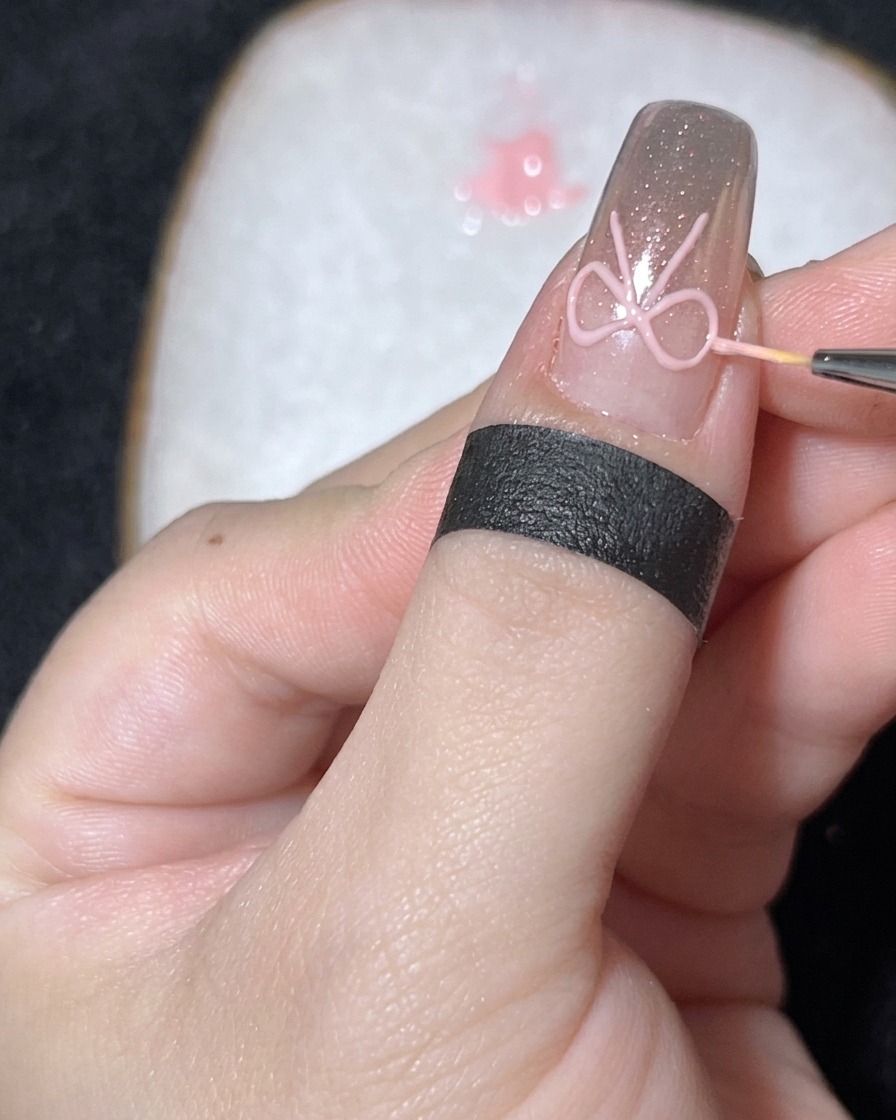 Gros plan dun pinceau fin plaçant une petite perle blanche au centre dun nœud en gel 3D sur un ongle chromé.