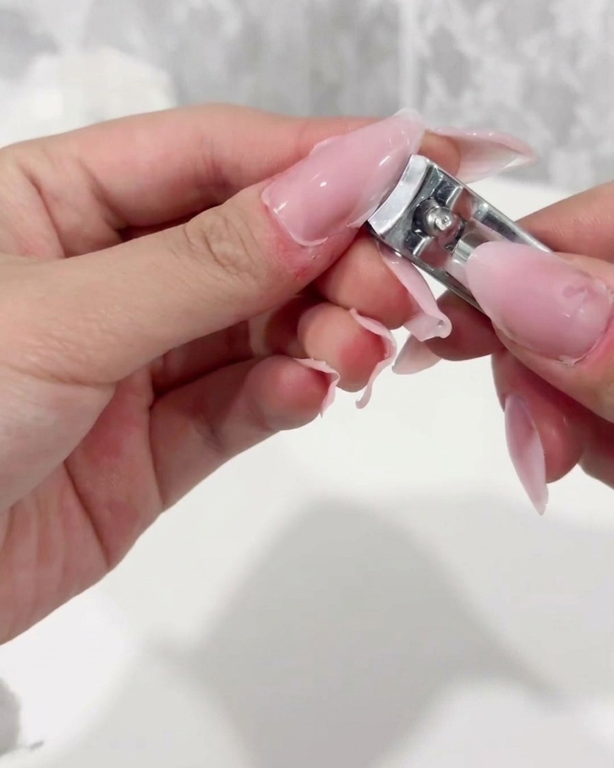 Un coupe-ongles coupant le bord libre dune capsule dextension en plastique transparent.