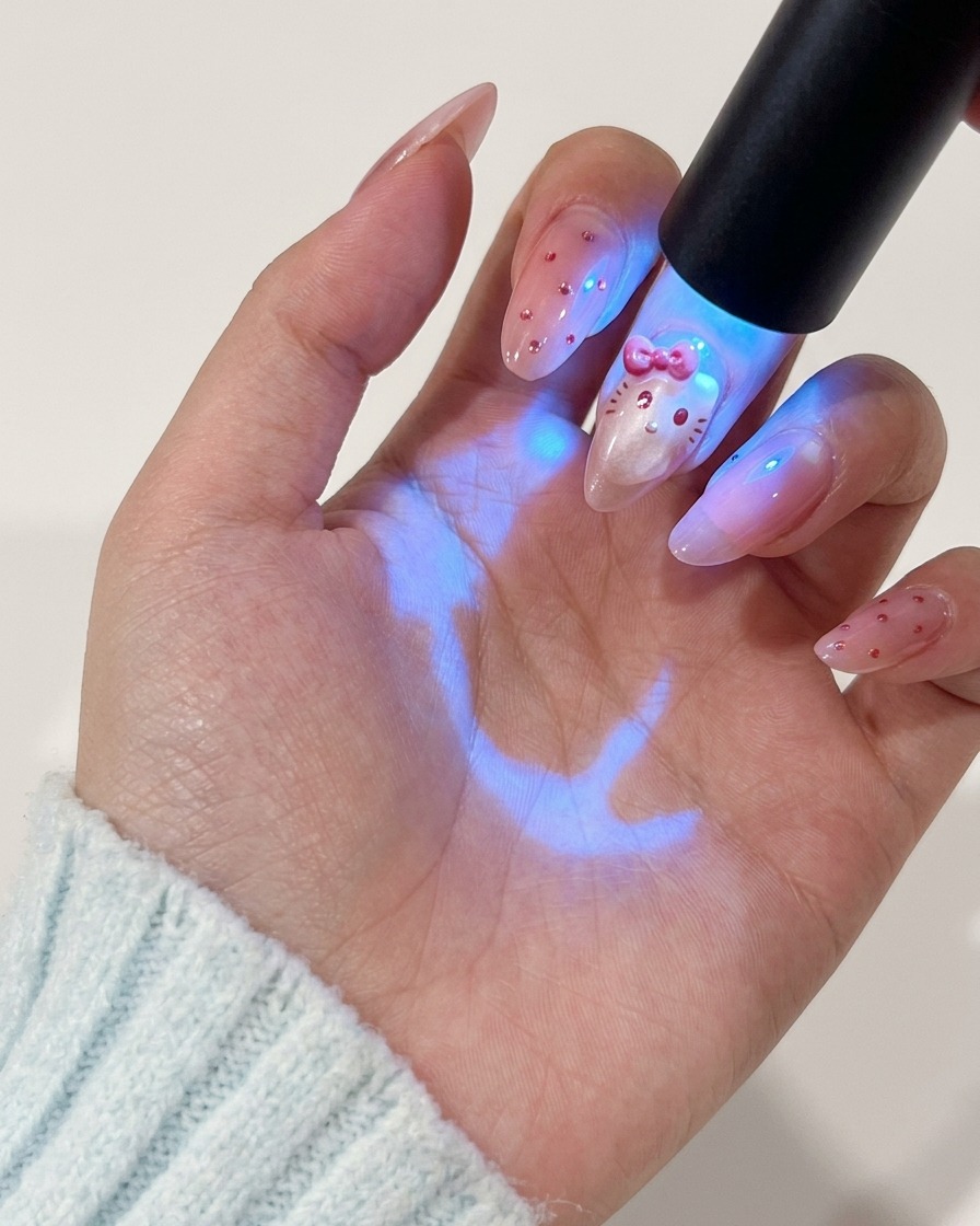 Une main tenant une lampe UV au-dessus de longle pour catalyser le design du personnage peint en rouge.